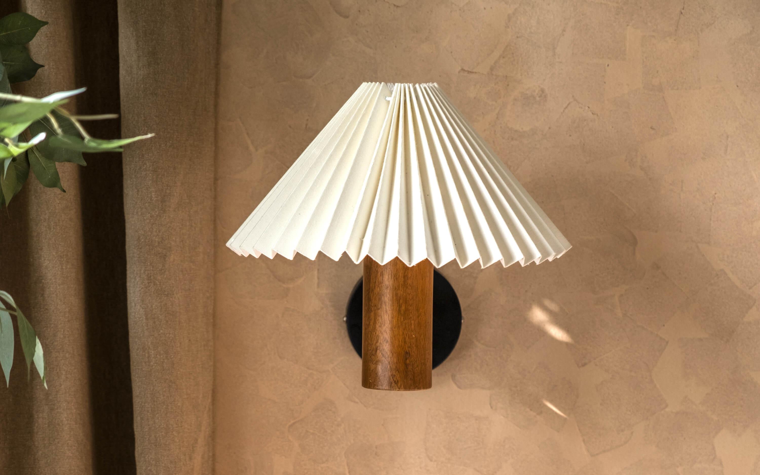 White pleated shade wall lamp with a natural wooden cylindrical base in walnut finish, perfect as a bedside wall lamp or decorative wall sconce for minimalist and vintage interiors.